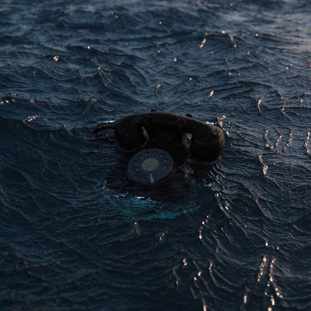 Old rotary telephone partially submerged in dark water with rippling surface.