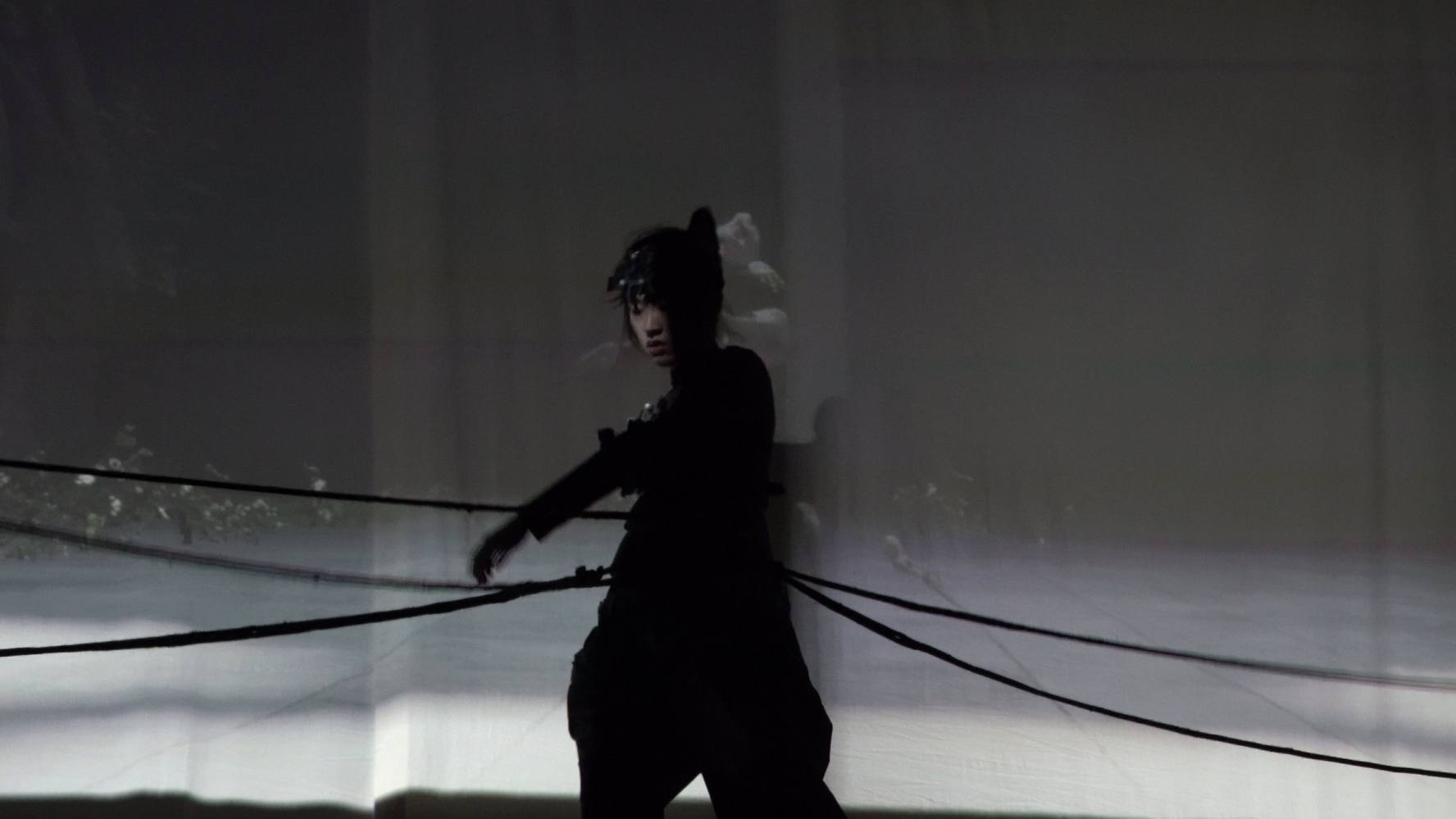 Silhouetted person in dark clothing standing amidst horizontal ropes against a foggy backdrop.